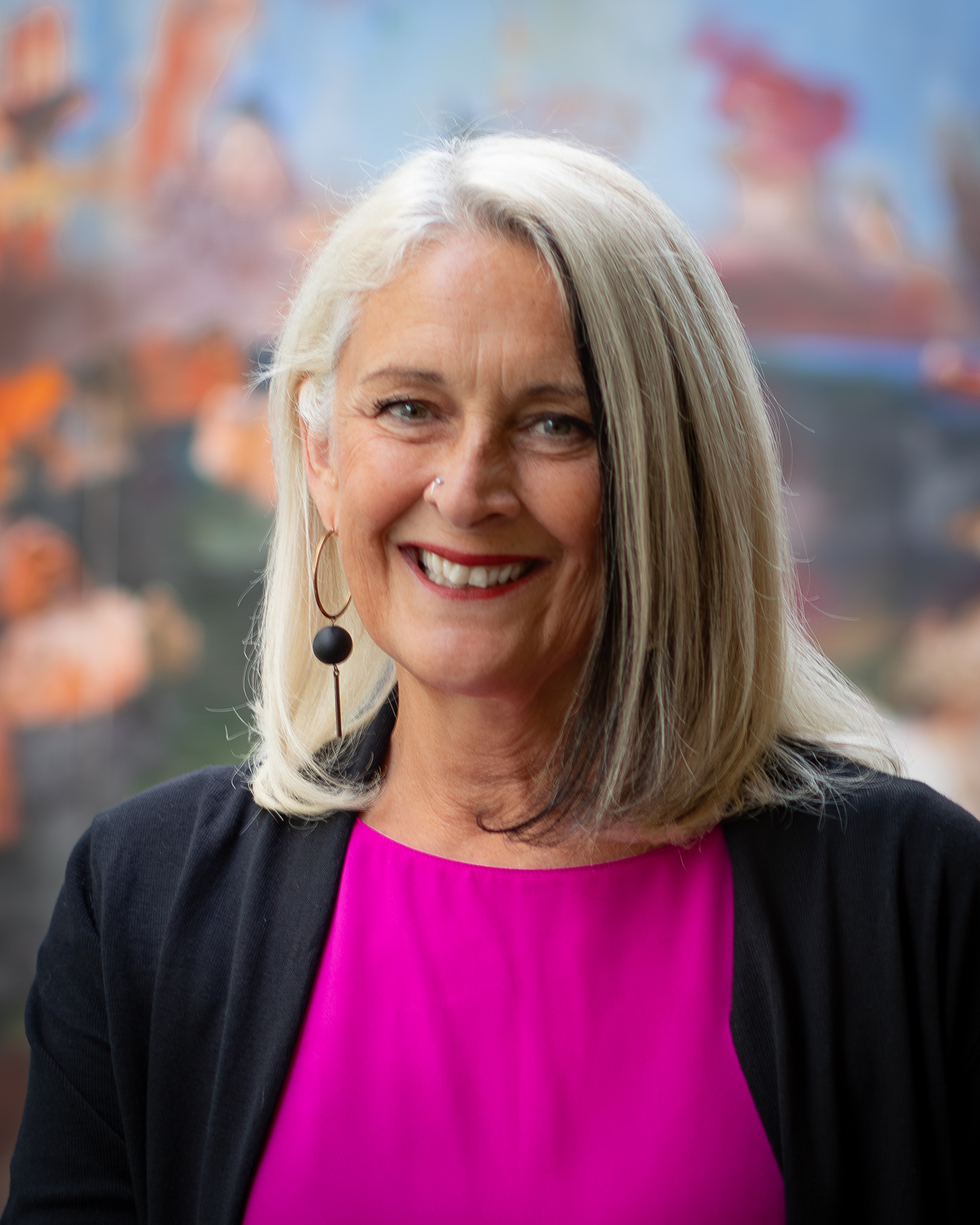 A woman in pink and black top in front of a colorful background