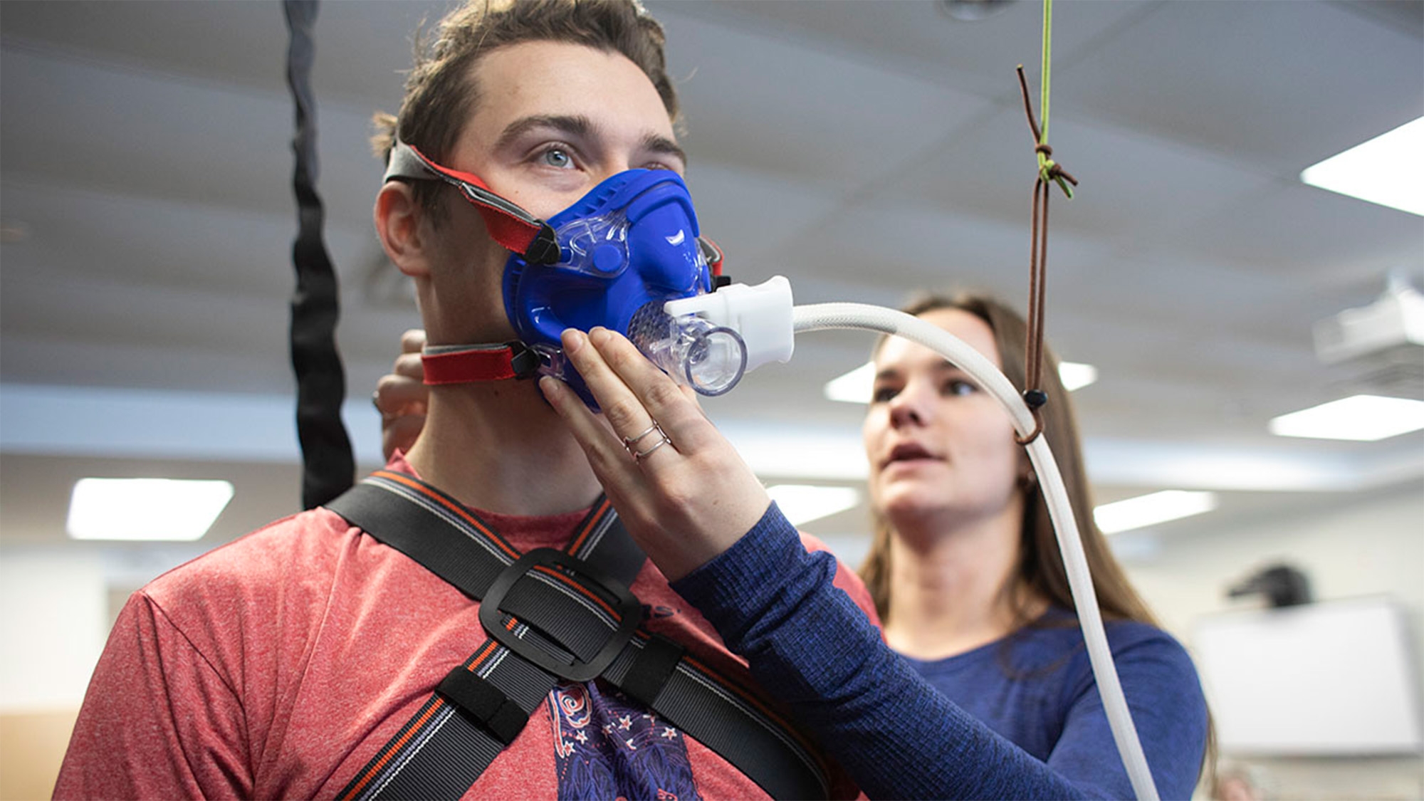 A female student in navy putting a breathing mask on a male student in red