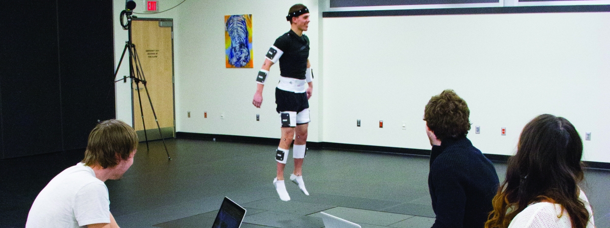 A student jumping with gears attached while 3 other students observe him