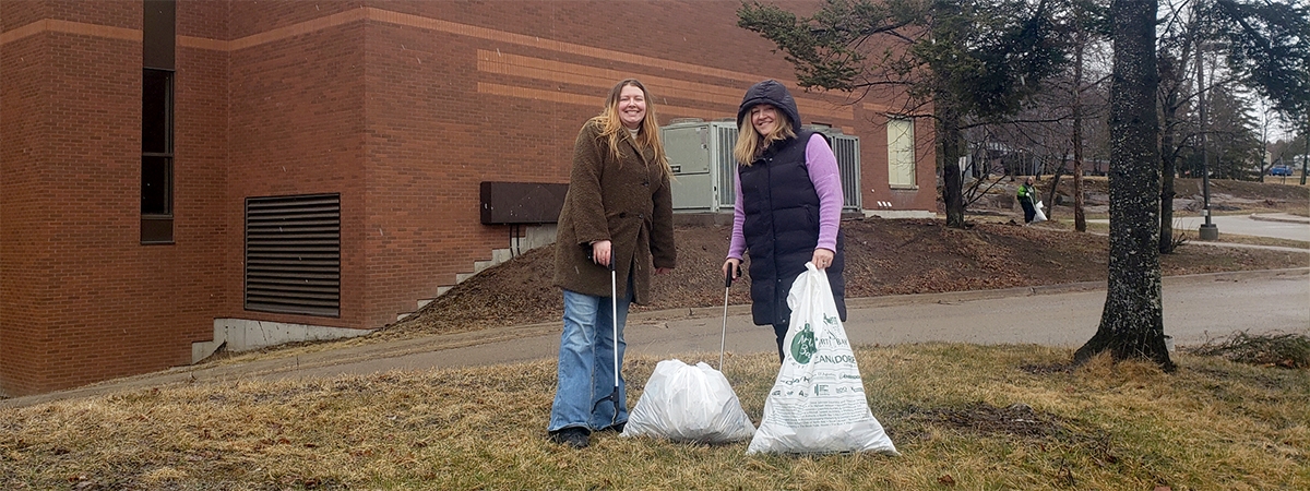 Two Nipissing staff members in front of the building with trash bags and grabbers