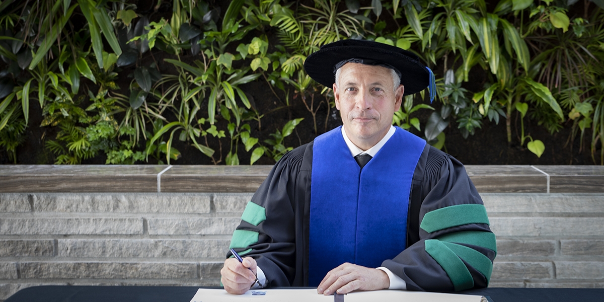 President Kevin Wamsley sitting at a table signing the register following his installation.