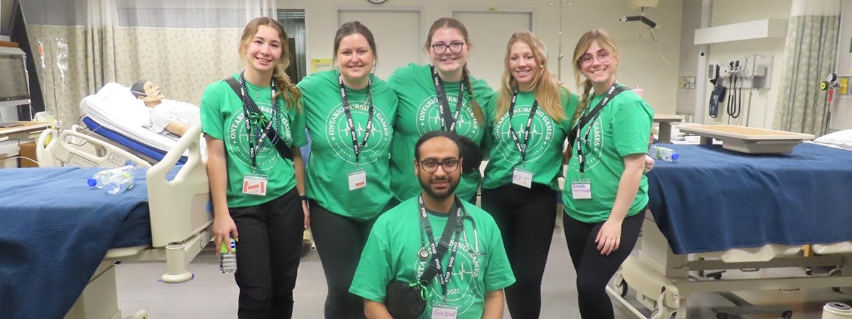 NU student group photo at the Nursing games, standing in a hospital simulation setting. 